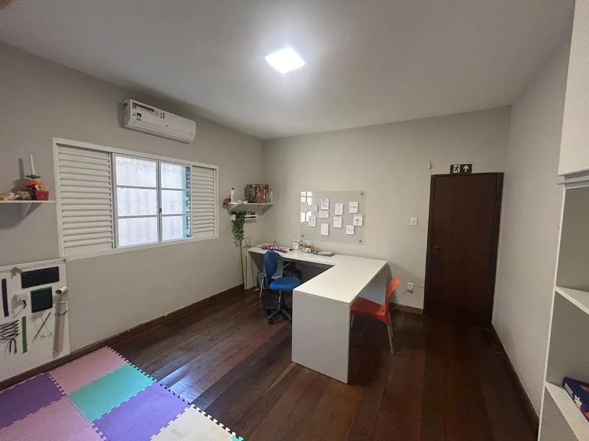 Sala de atendimento com mesa em L, cadeiras infantis, tapete de tatame colorido e prateleira com jogos pedagógicos
